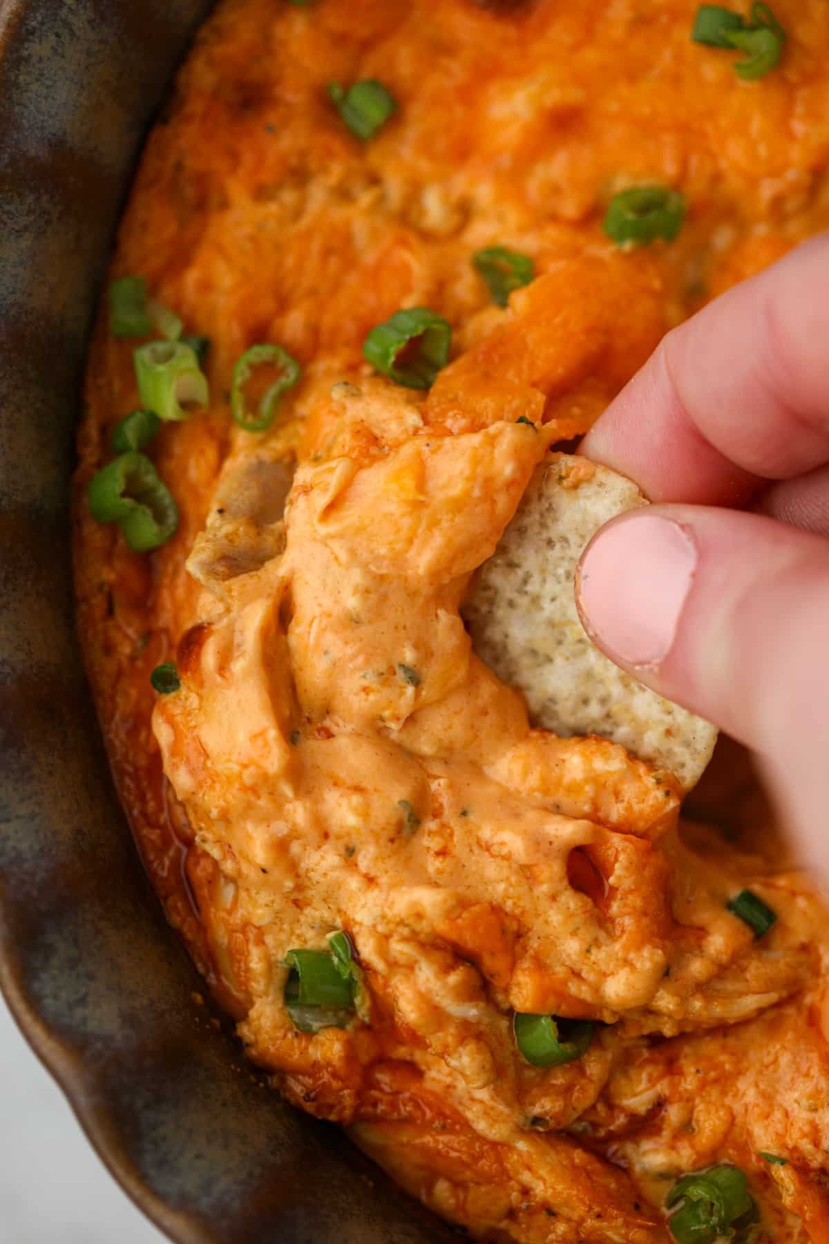 Dipping a tortilla chip into a brightly colored buffalo chicken dip.