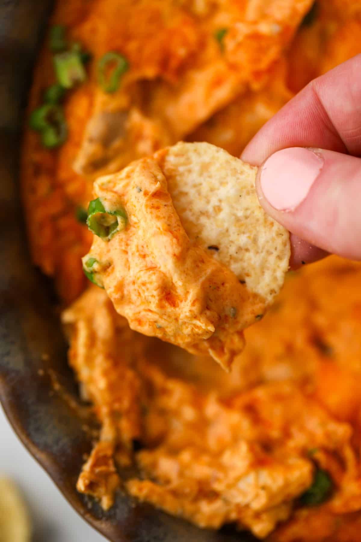 Dipping a tortilla chip into a bubbly buffalo chicken dip.