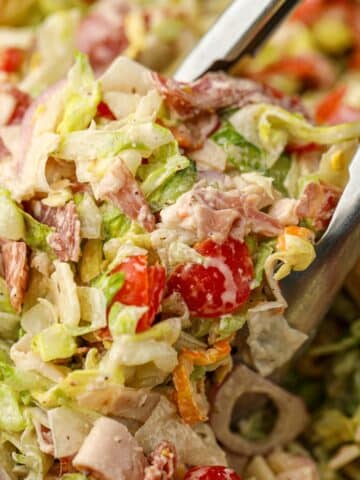 A pair of tongs picking up a portion of chopped Italian salad.