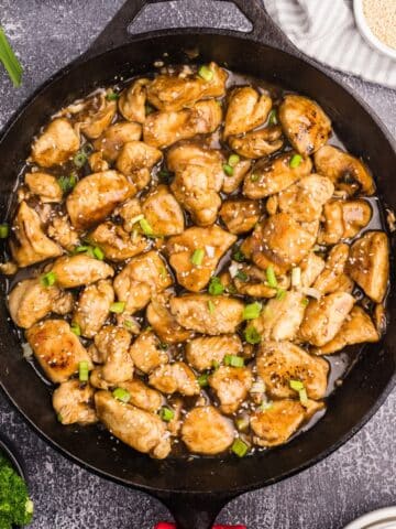 A skillet filled with cooked chicken stir fry with a golden sauce.