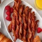 A platter full of twisted bacon/bacon twists, garnished with fresh raspberries.