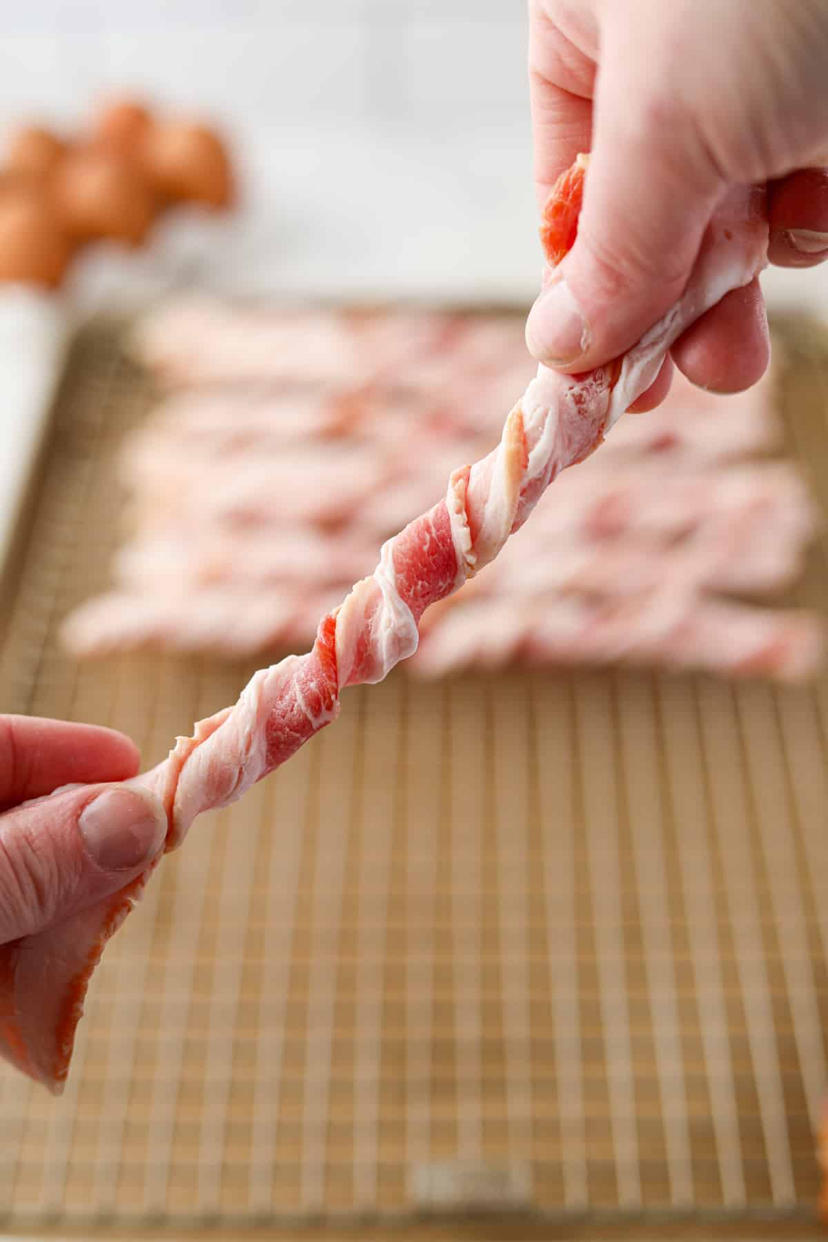 Using both hands to twist a slice of bacon into a spiral.
