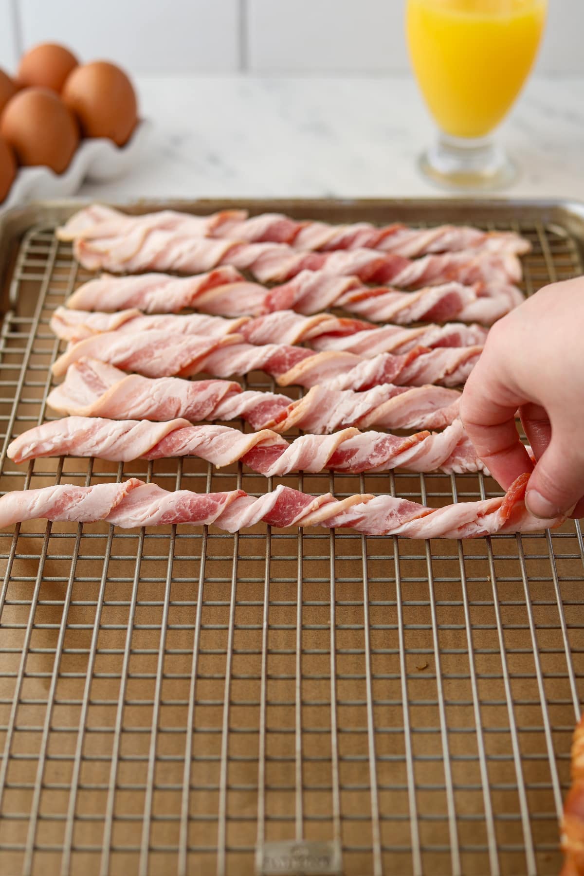 Placing spiral bacon slices on a wire rack set inside of a baking sheet.