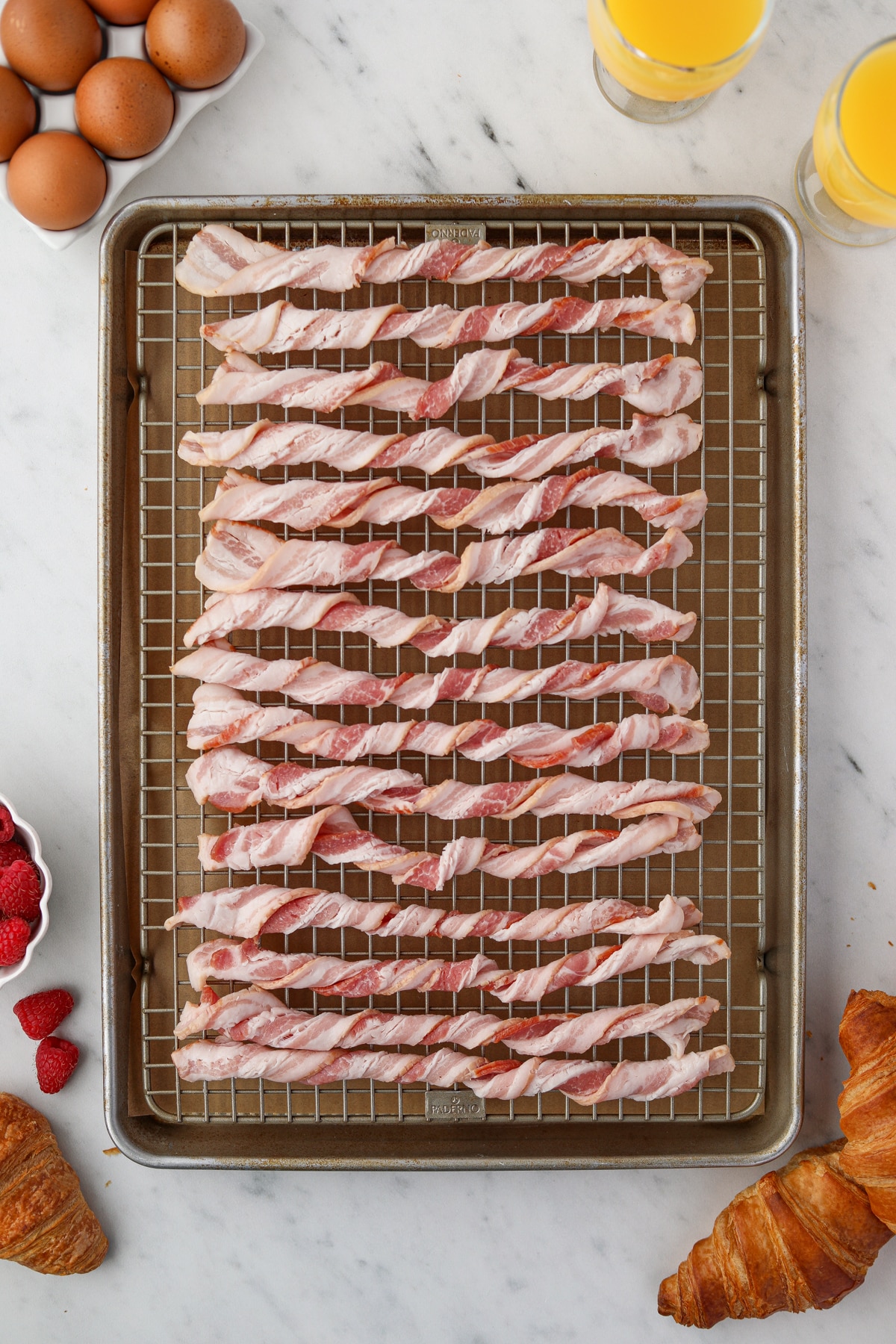 A baking sheet with a wire baking rack filled with twisted raw bacon slices.