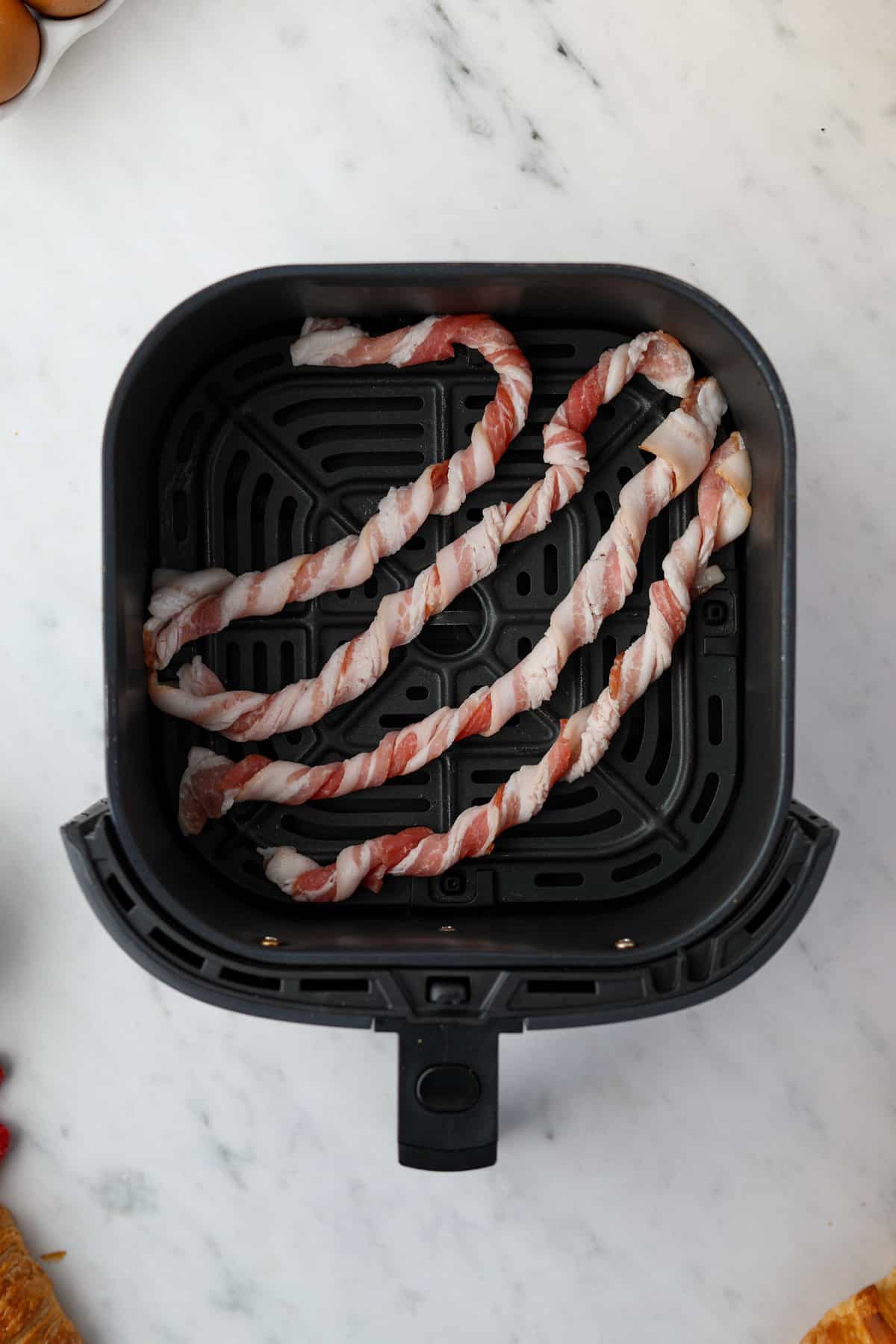 An air fryer with 4 bacon spirals set inside, bent slightly.