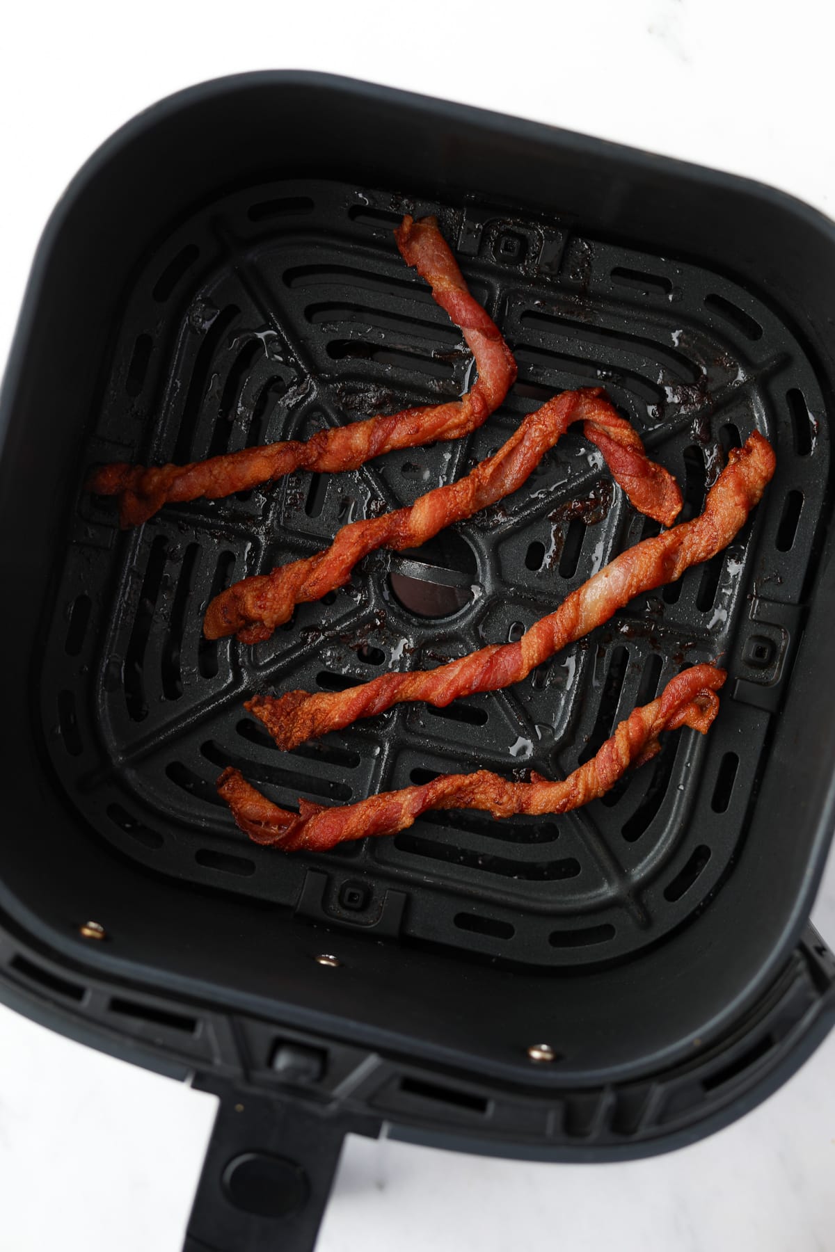 An air fryer basket with 4 cooked twisted bacon pieces inside.