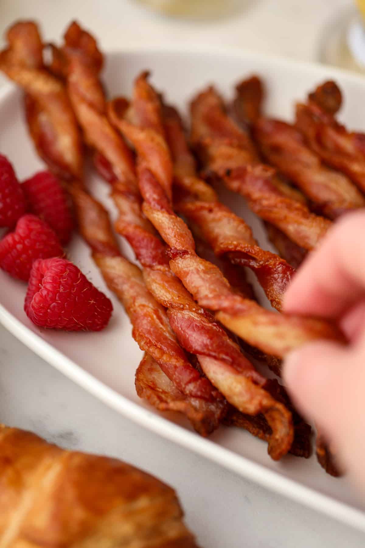 A hand taking a single bacon twist from a large platter full.