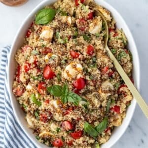 A large bowl filled with quinoa salad, garnished with fresh basil, sliced mini mozzarella, and balsamic glaze.