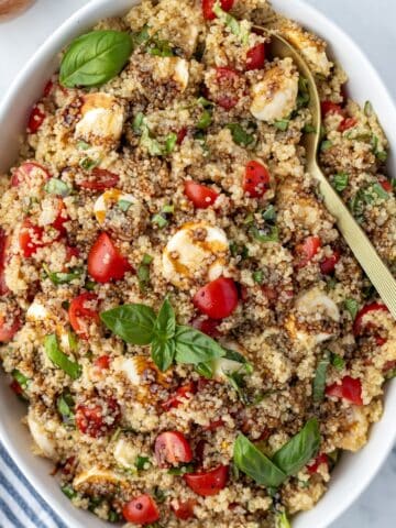 A large bowl filled with quinoa salad, garnished with fresh basil, sliced mini mozzarella, and balsamic glaze.