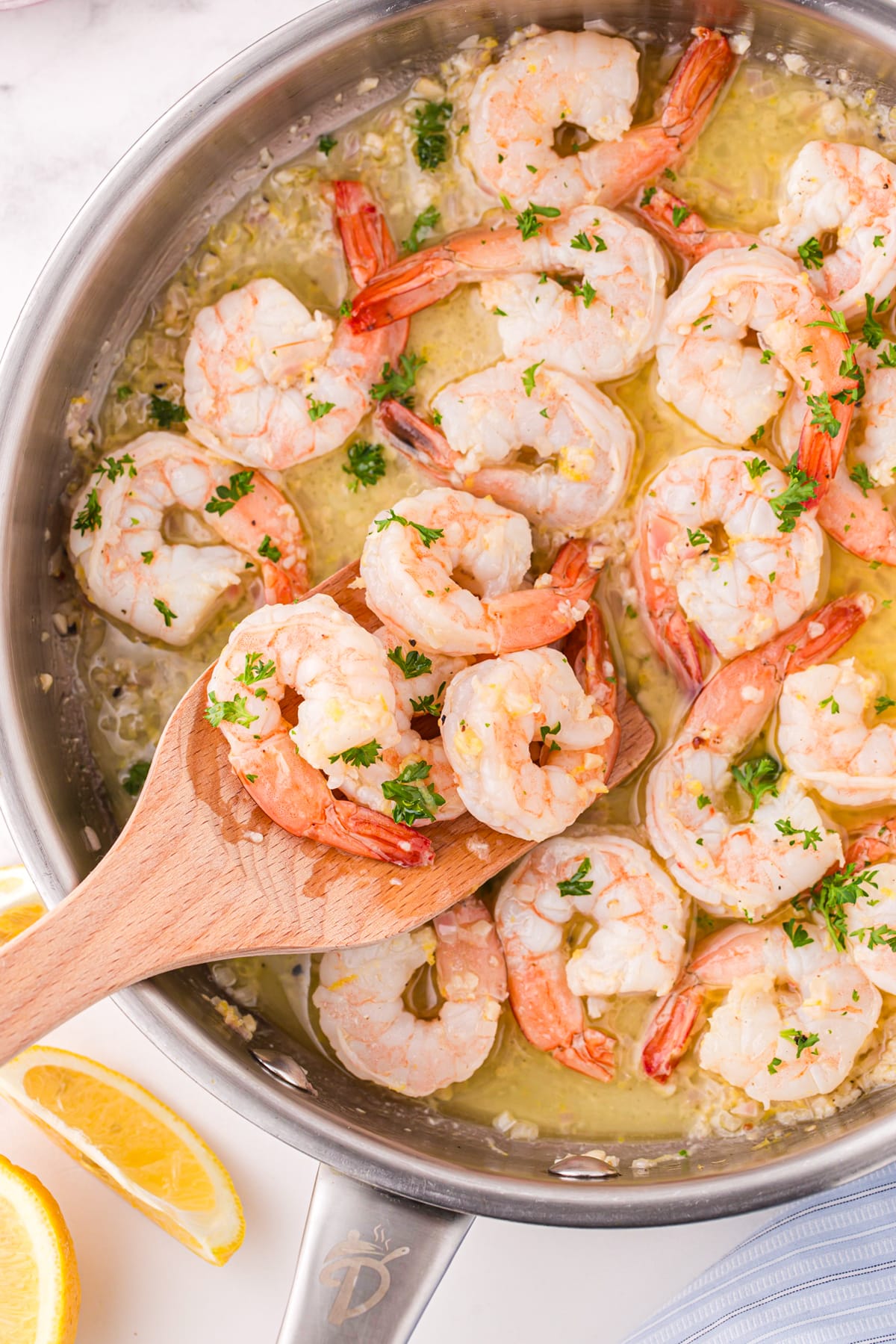 A wooden spatula scooping shrimp from a skillet.