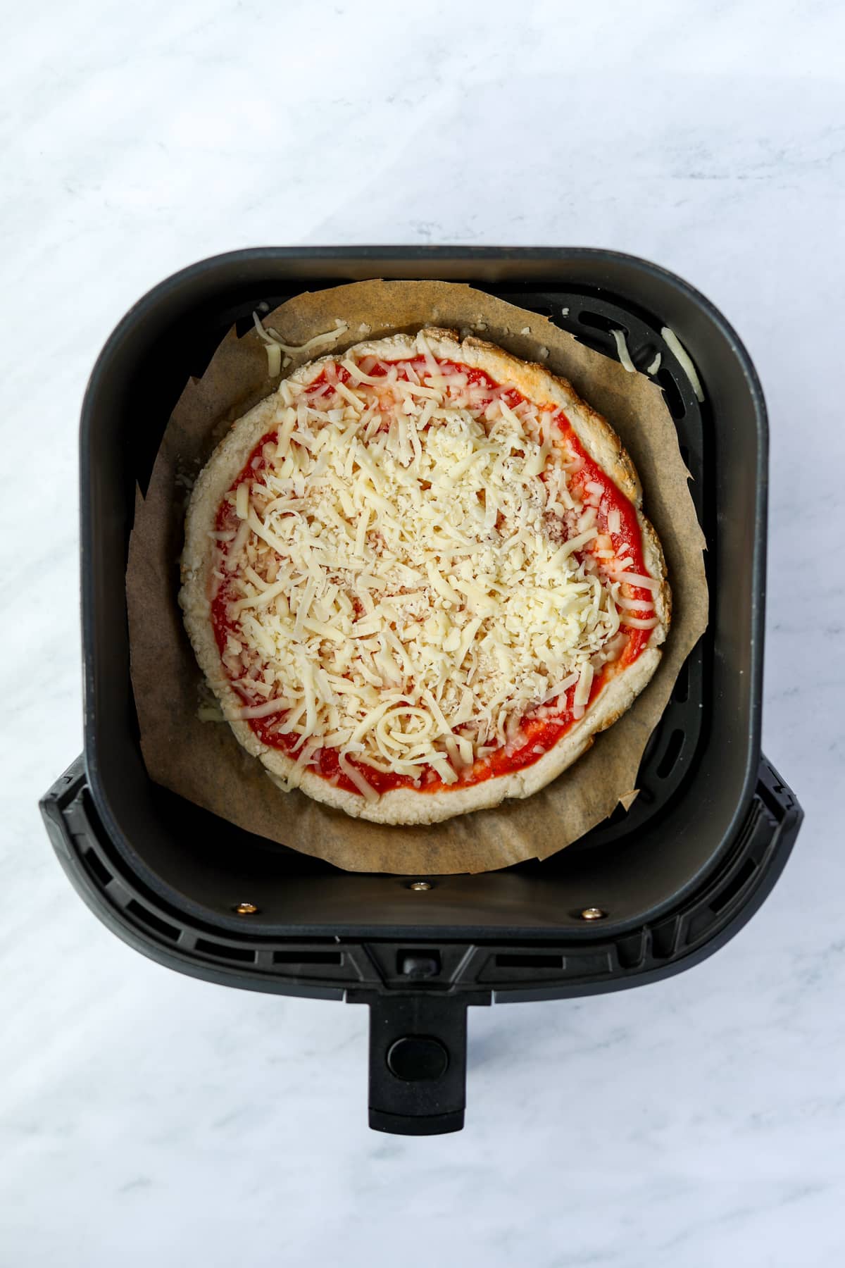 An air fryer with an uncooked mini pizza inside.