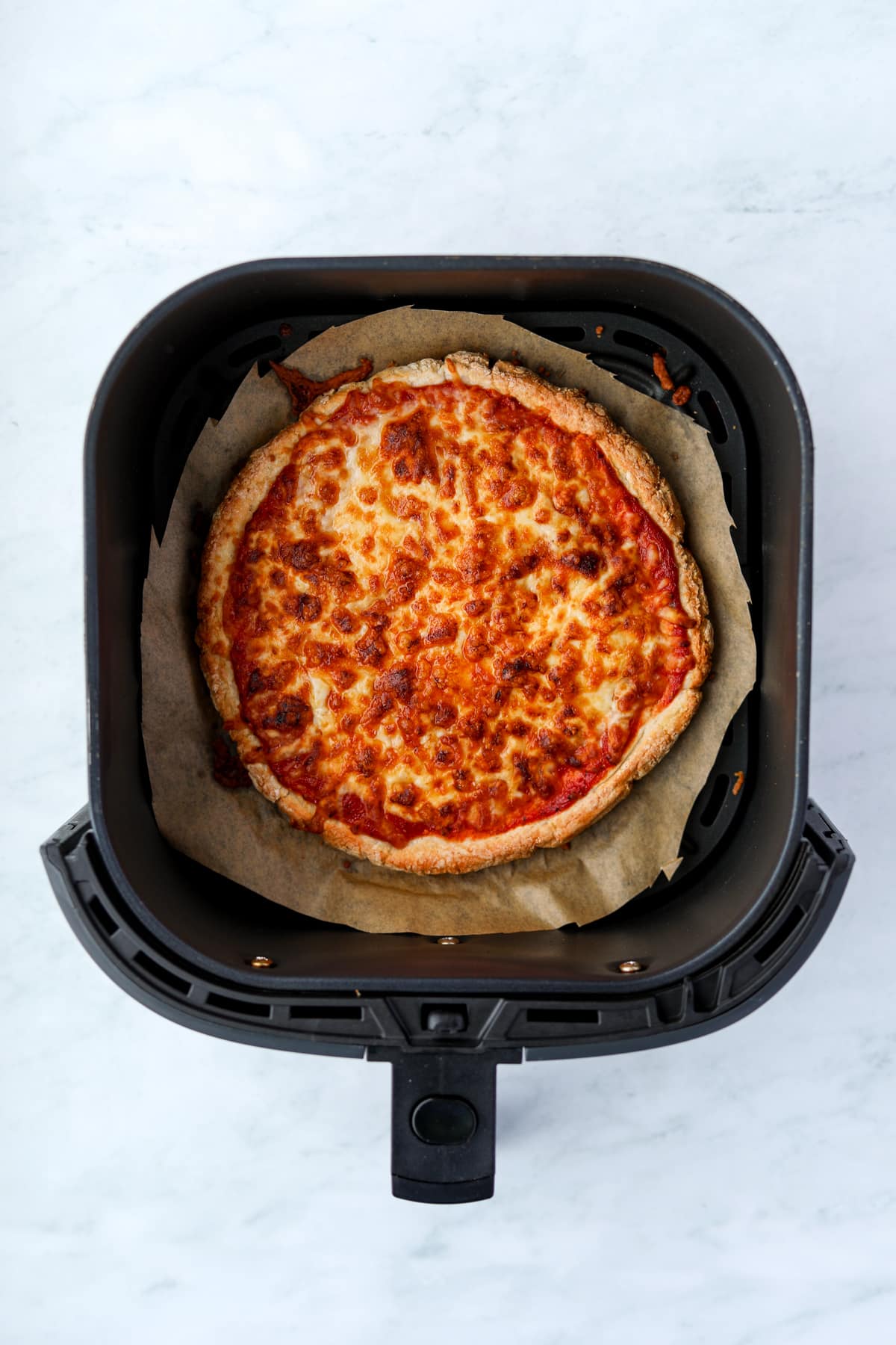 An air fryer with a cooked cheese pizza inside.
