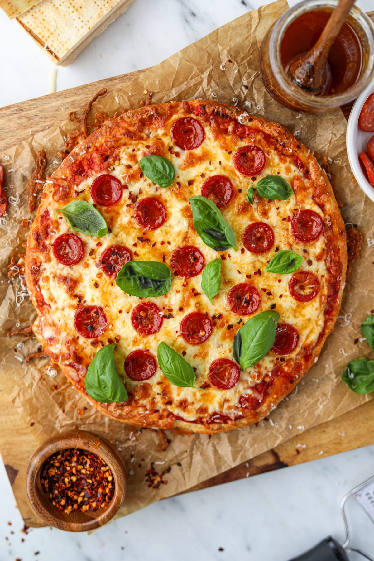 Pizza on a sheet of parchment paper, topped with pepperoni, fresh basil, and crushed red pepper.