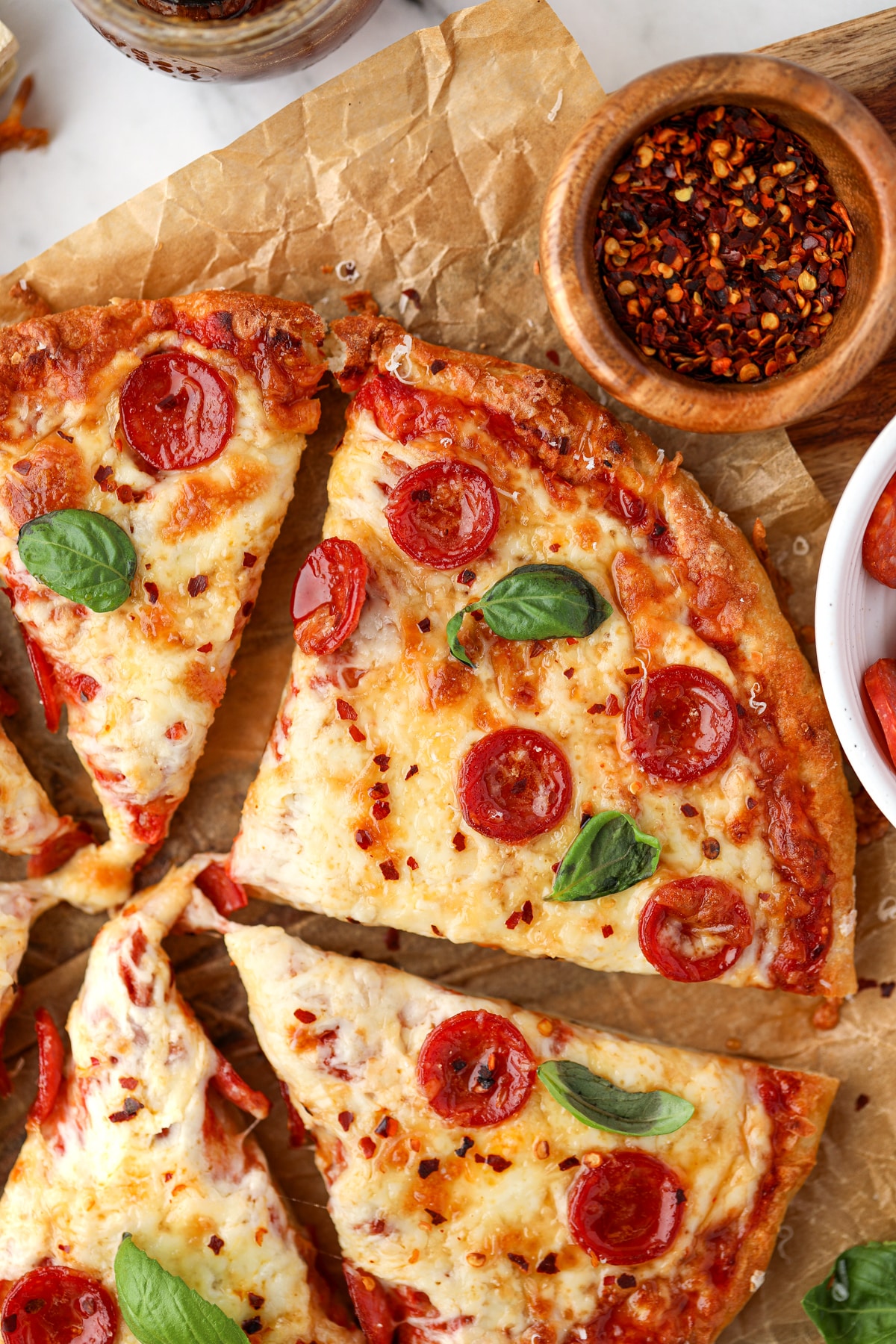 Slices of pizza on a sheet of parchment paper, topped with pepperoni and fresh basil/