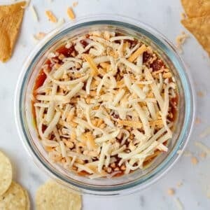A bowl of dip with salsa, Greek yogurt, and topped with shredded cheese.