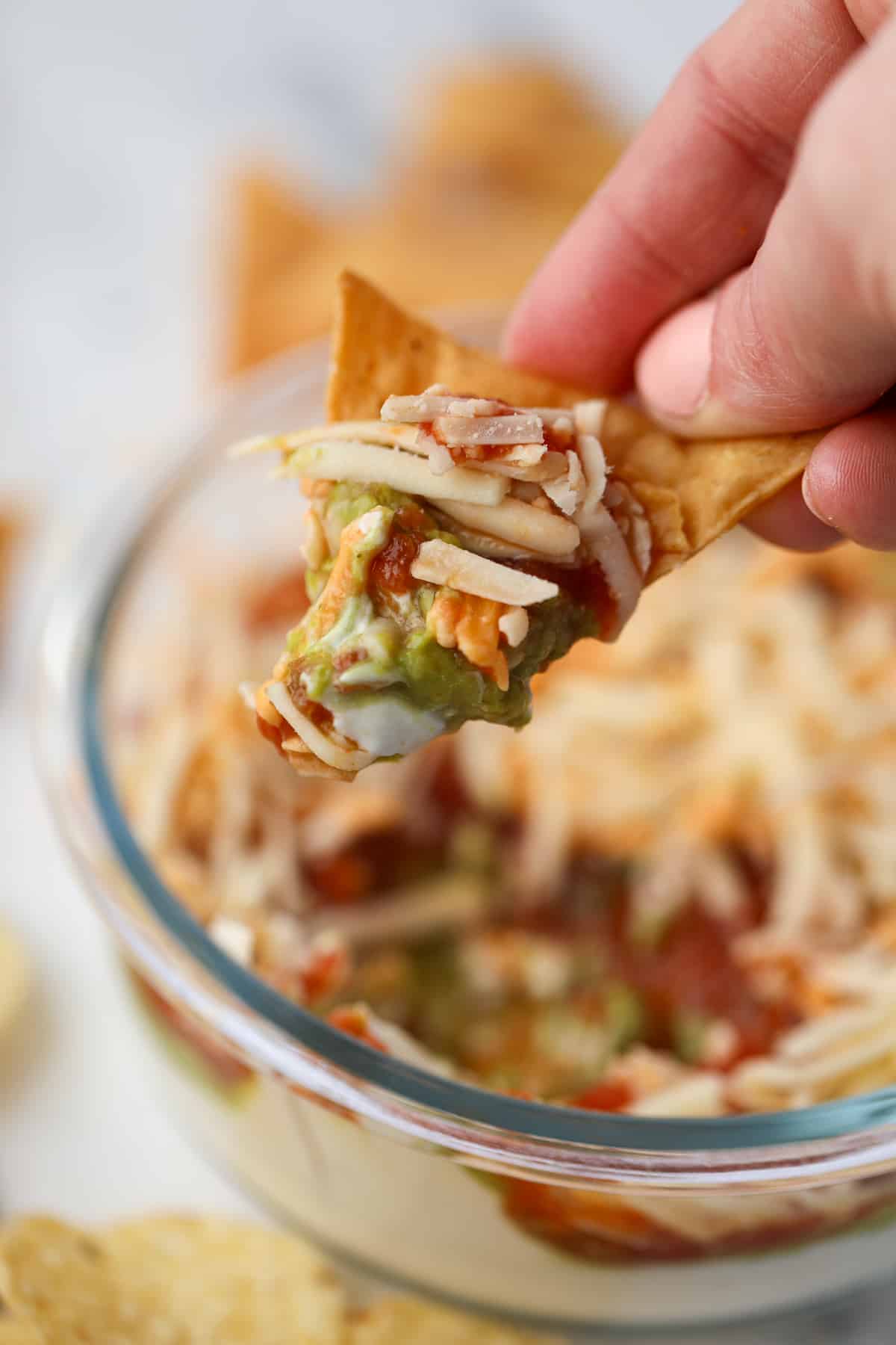 A tortilla chip with guacamole, salsa, shredded cheese, and Greek yogurt. 