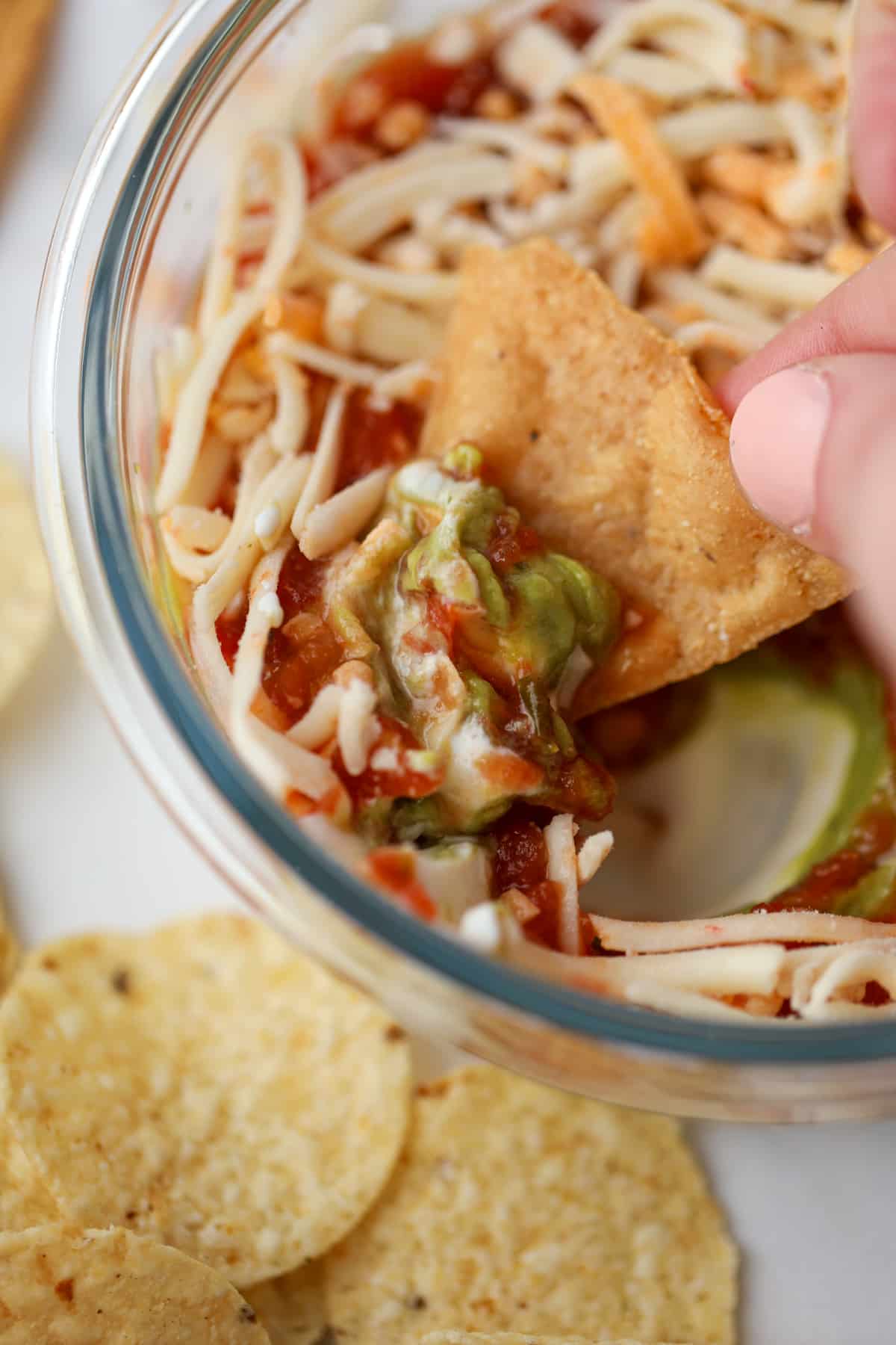 A tortilla chip being dipped into a small bowl of layered dip.