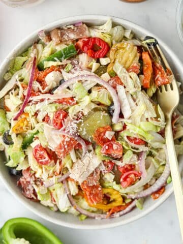 A bowl filled with salad, topped with pickles, red onion, cherry tomatoes, and a sprinkle of parmesan cheese.