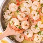 A wooden spatula scooping shrimp cooked in a lemon garlic butter sauce.