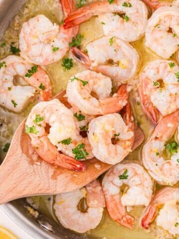 A wooden spatula scooping shrimp cooked in a lemon garlic butter sauce.