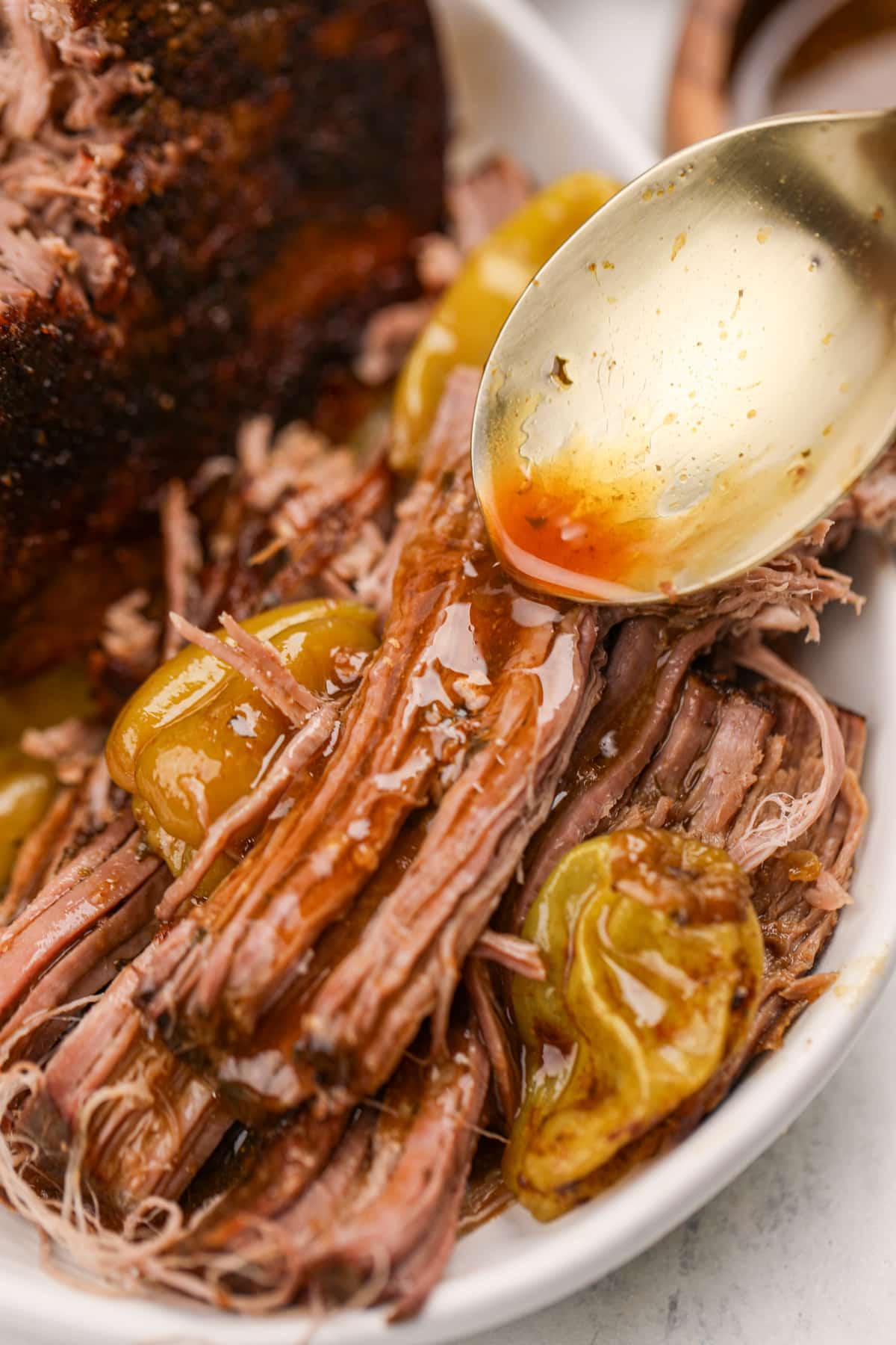 Spooning reserved juices over shredded pot roast.