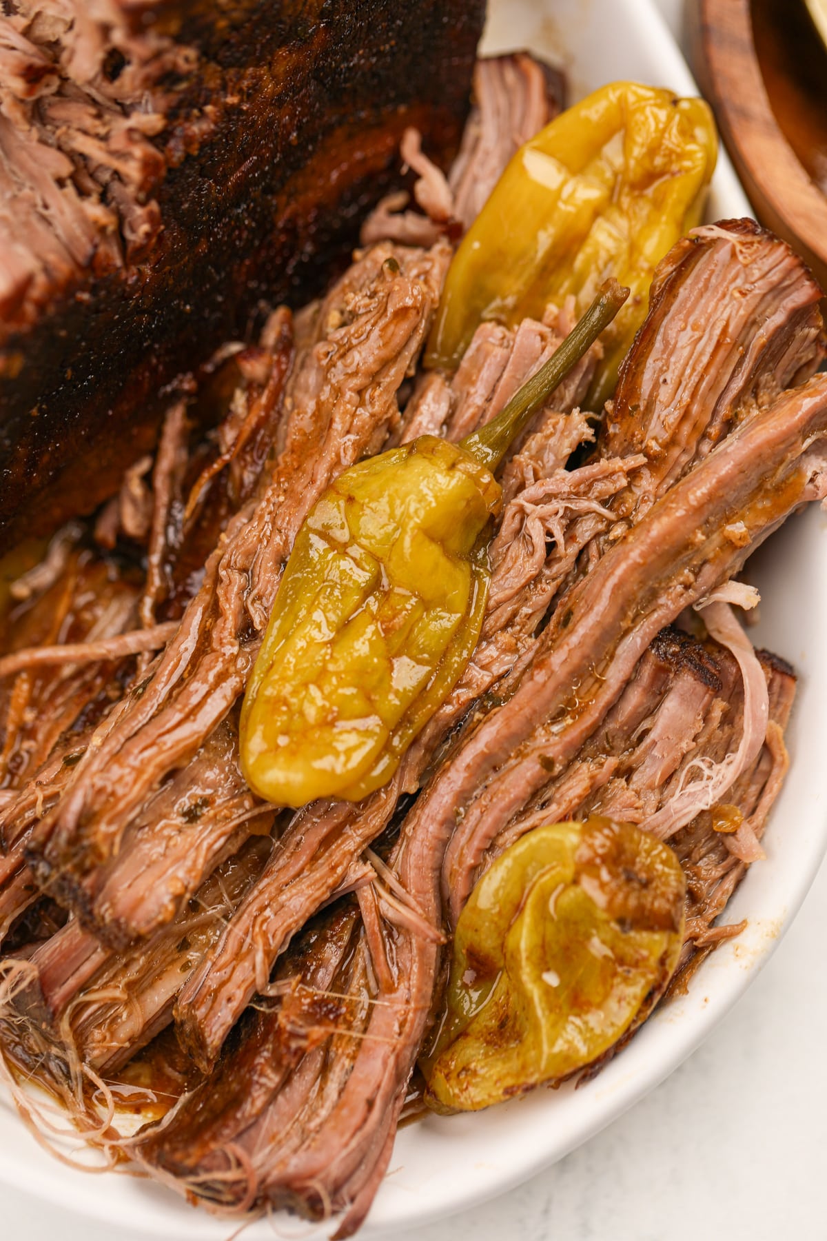 Shredded pot roast with cooked pepperoncini peppers alongside it.