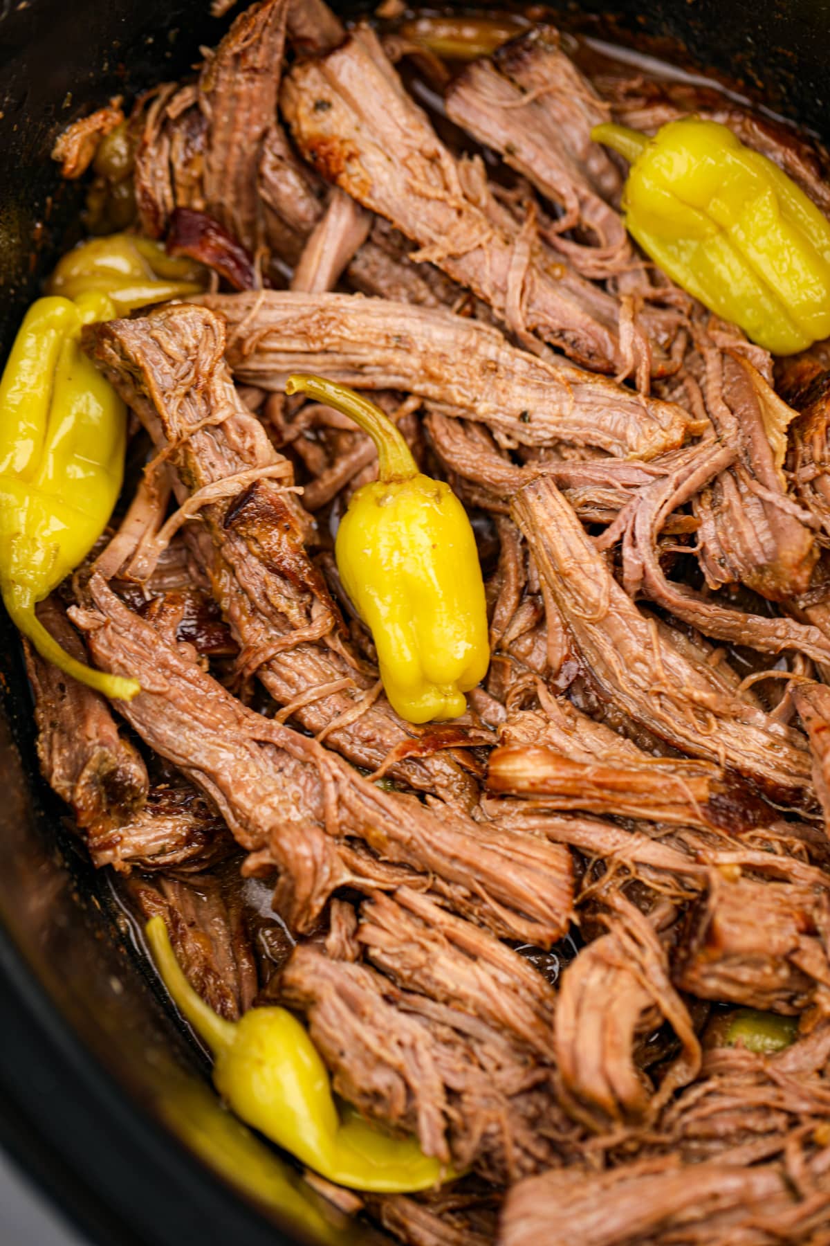 Shredded pot roast in a slow cooker, garnished with mini peppers. 