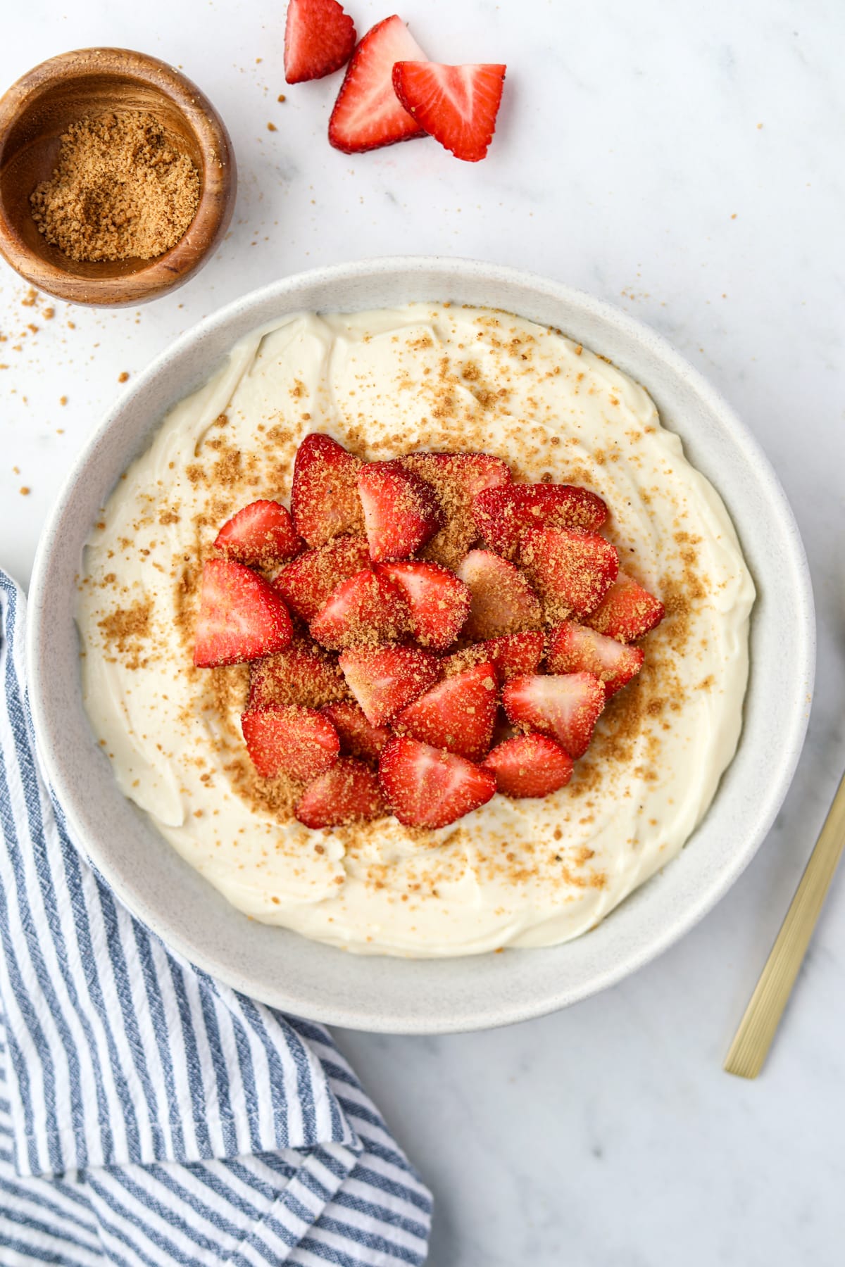 A bowl of yogurt topped with strawberries and graham cracker crumbs.