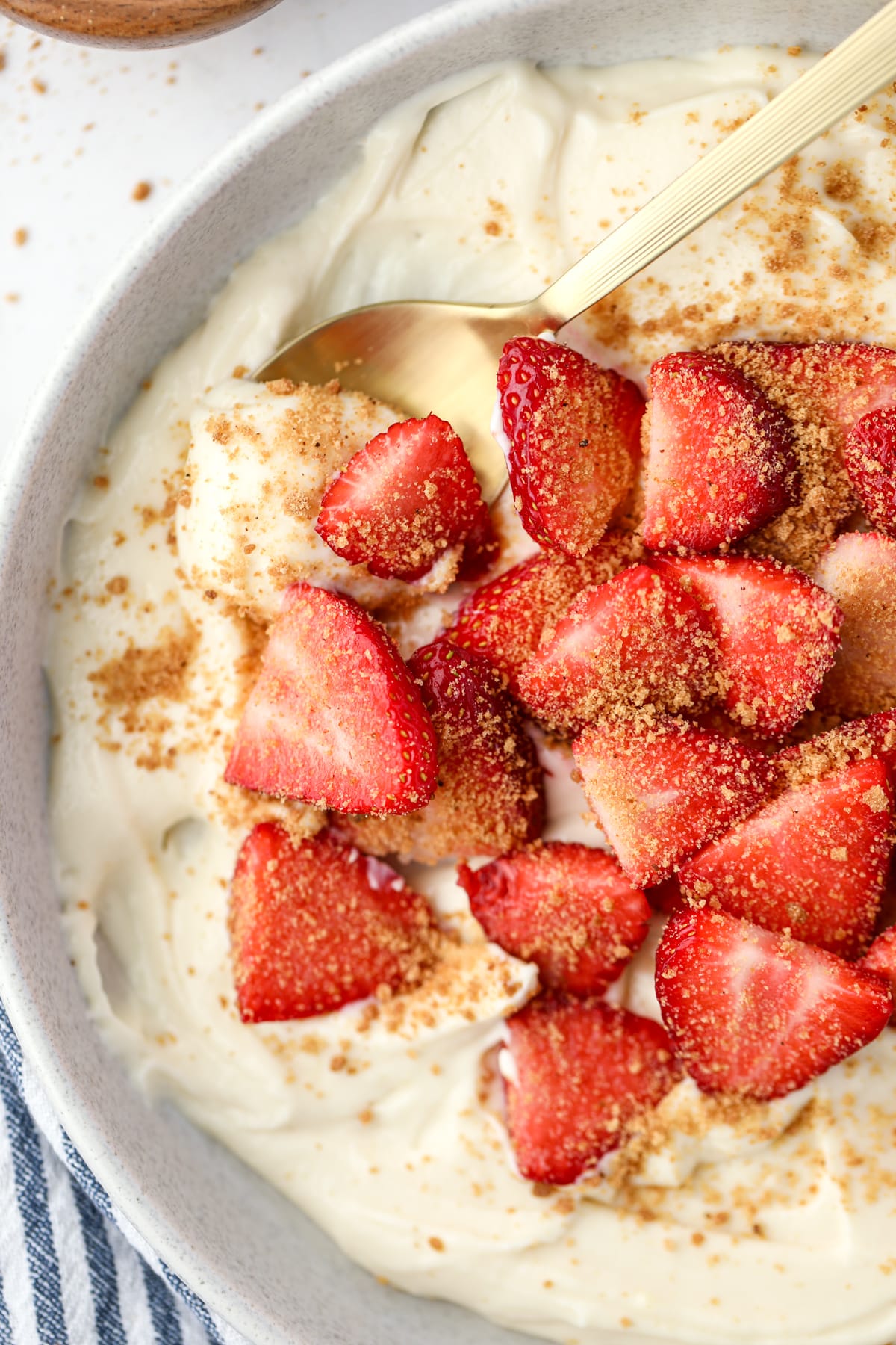 A spoon scooping creamy yogurt from a bowl topped with fresh sliced strawberries.