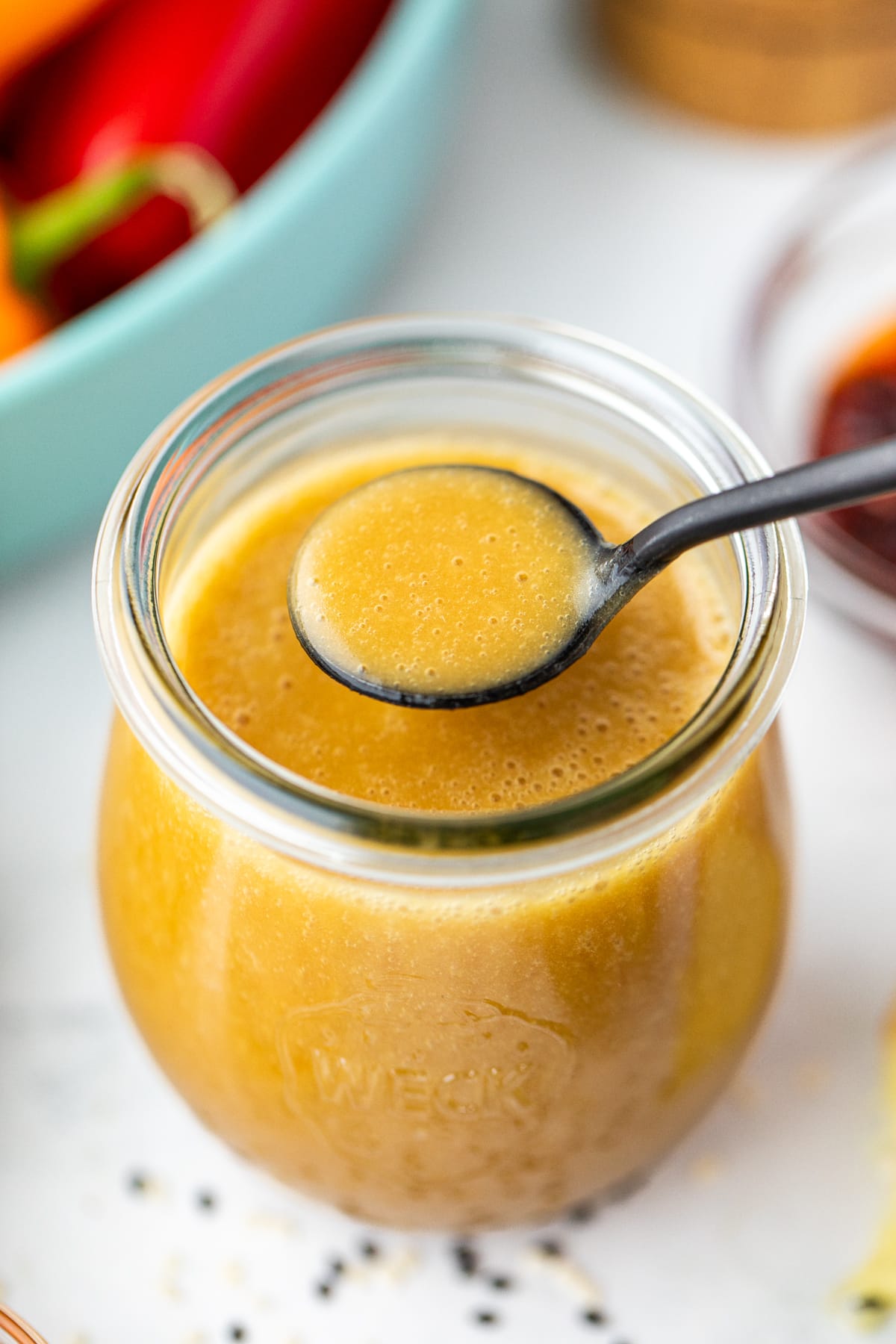 A spoon taking a small amount of homemade vinaigrette from a small jar.