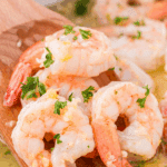 A wooden spatula scooping shrimp from a skillet, drenched in garlic butter sauce.
