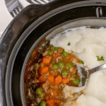 A ladle scooping into a slow cooker filled with homemade casserole.