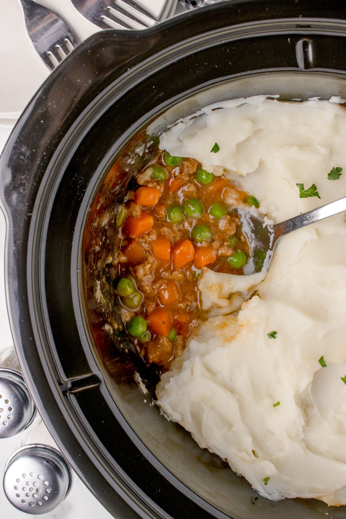 A slow cooker filled with cottage pie and topped with mashed potatoes.
