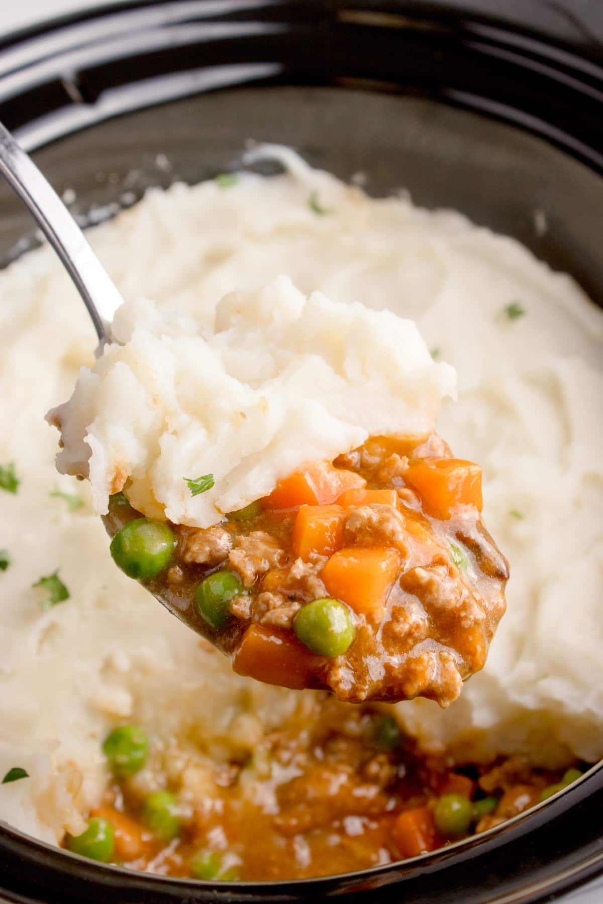 Taking a large scoop of shepherd's pie from a slow cooker.