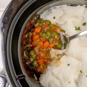 A slow cooker filled with shepherd's pie topped with mashed potatoes.