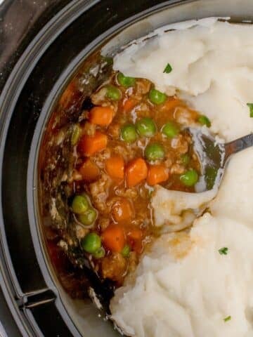 A slow cooker filled with shepherd's pie topped with mashed potatoes.
