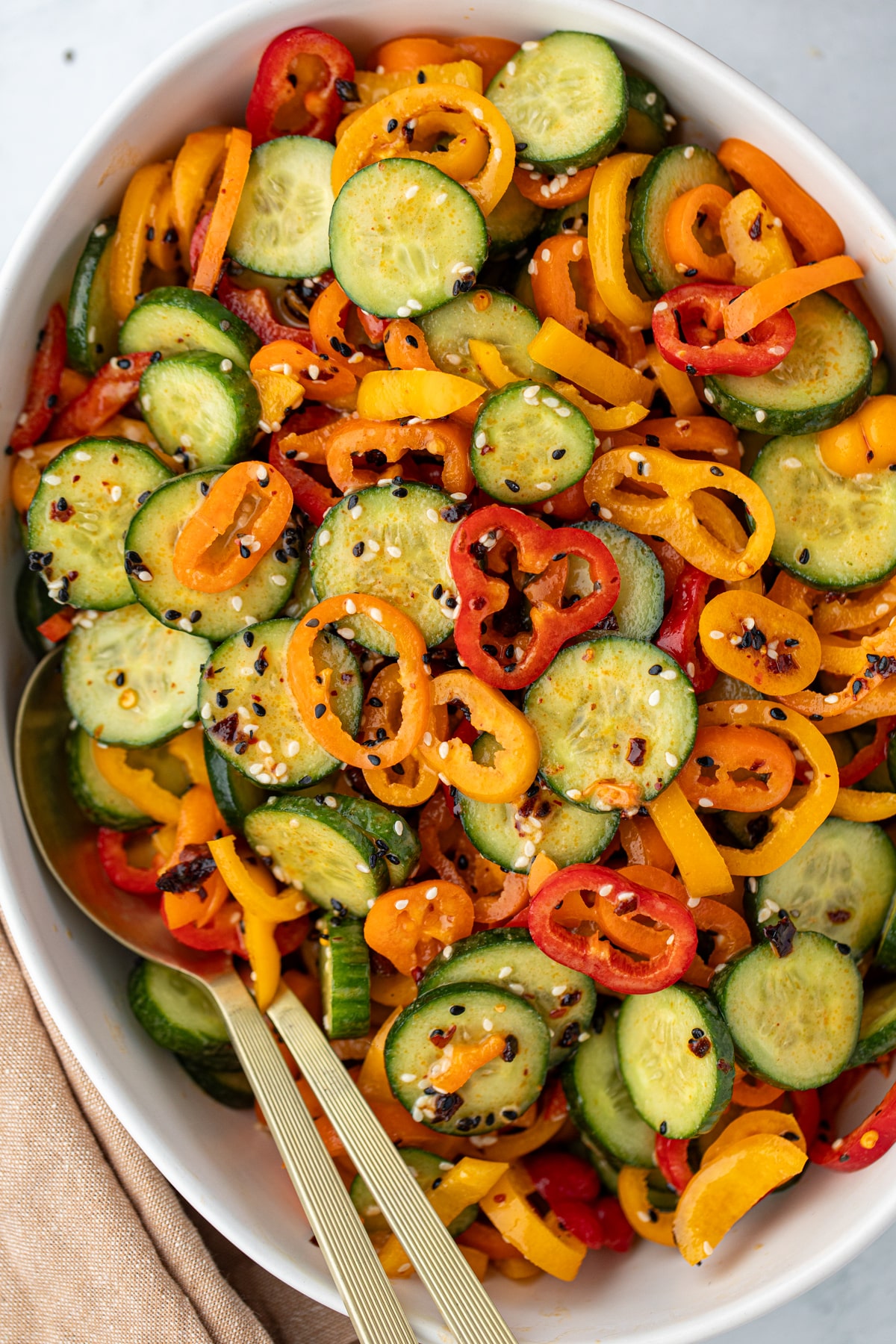 A bowl filled with cucumber and mini sliced bell pepper, topped with sesame seeds.