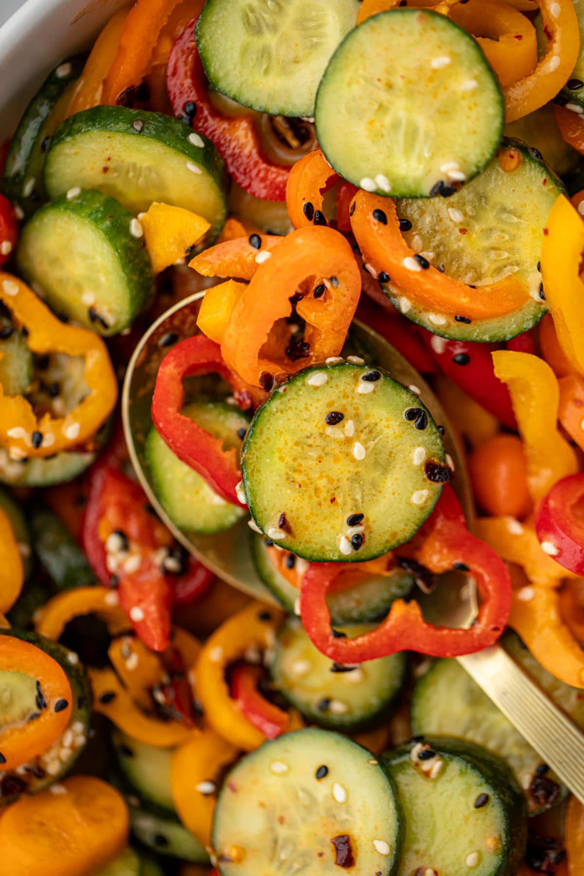 A spoon serving up a portion of cucumber and bell pepper salad.