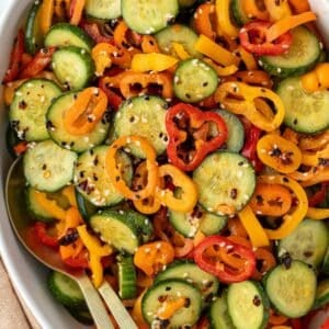 A bowl of sliced cucumber and sliced mini pepper tossed with dressing and a sprinkling of sesame seeds.