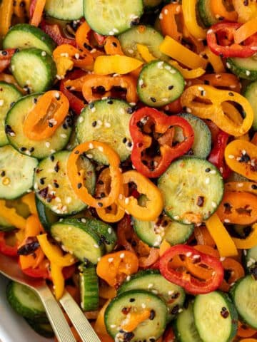 A bowl of sliced cucumber and sliced mini pepper tossed with dressing and a sprinkling of sesame seeds.