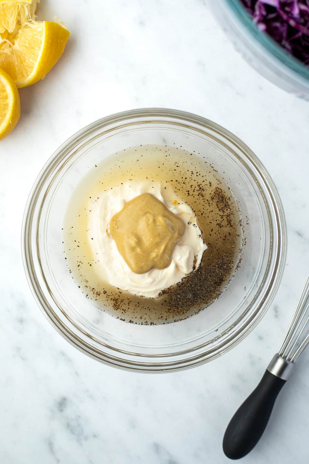 An overhead view of a bowl containing lemon juice, mayonnaise, dijon, and pepper. 