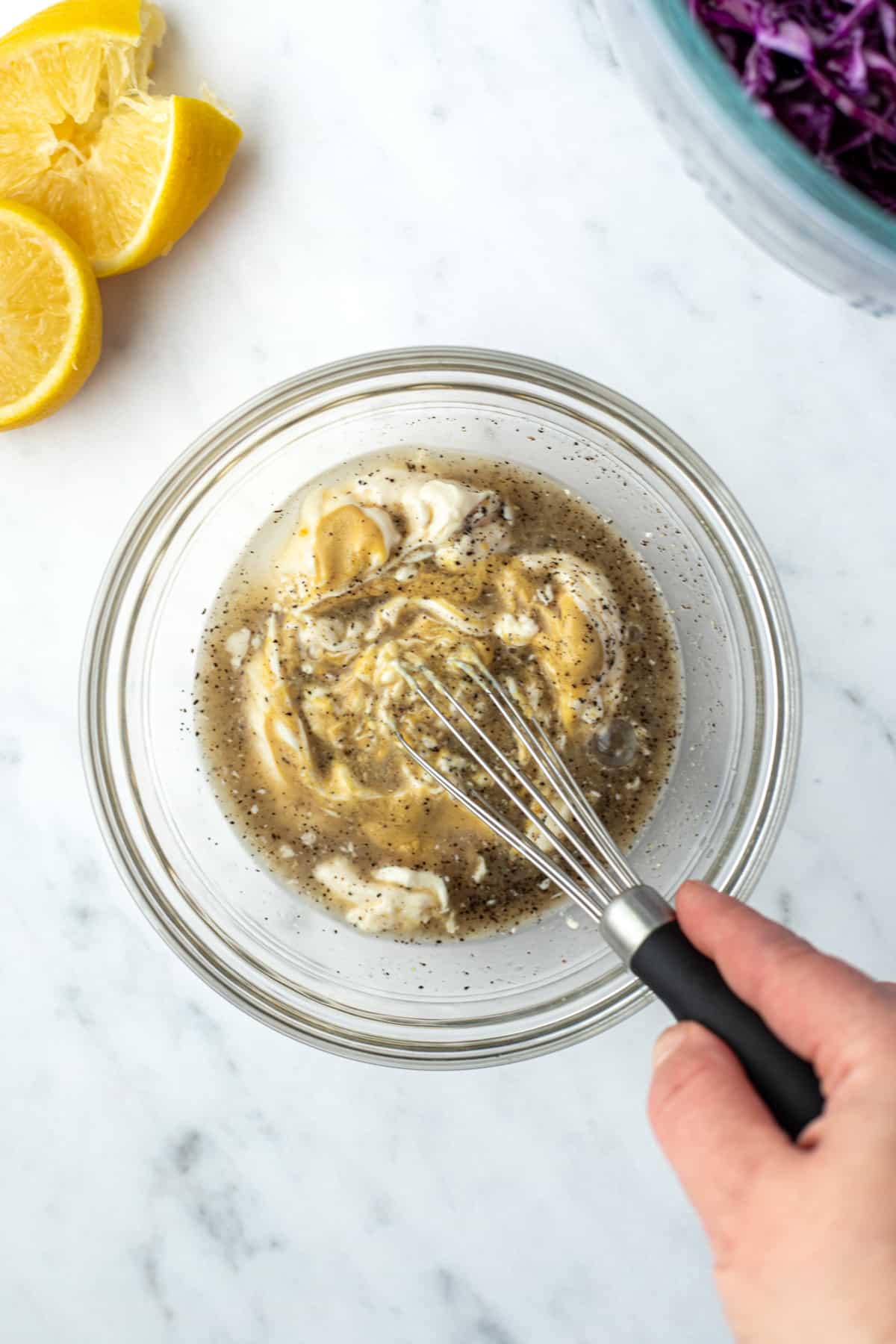 Whisking together mayo, lemon juice, dijon, and black pepper to make a dressing.