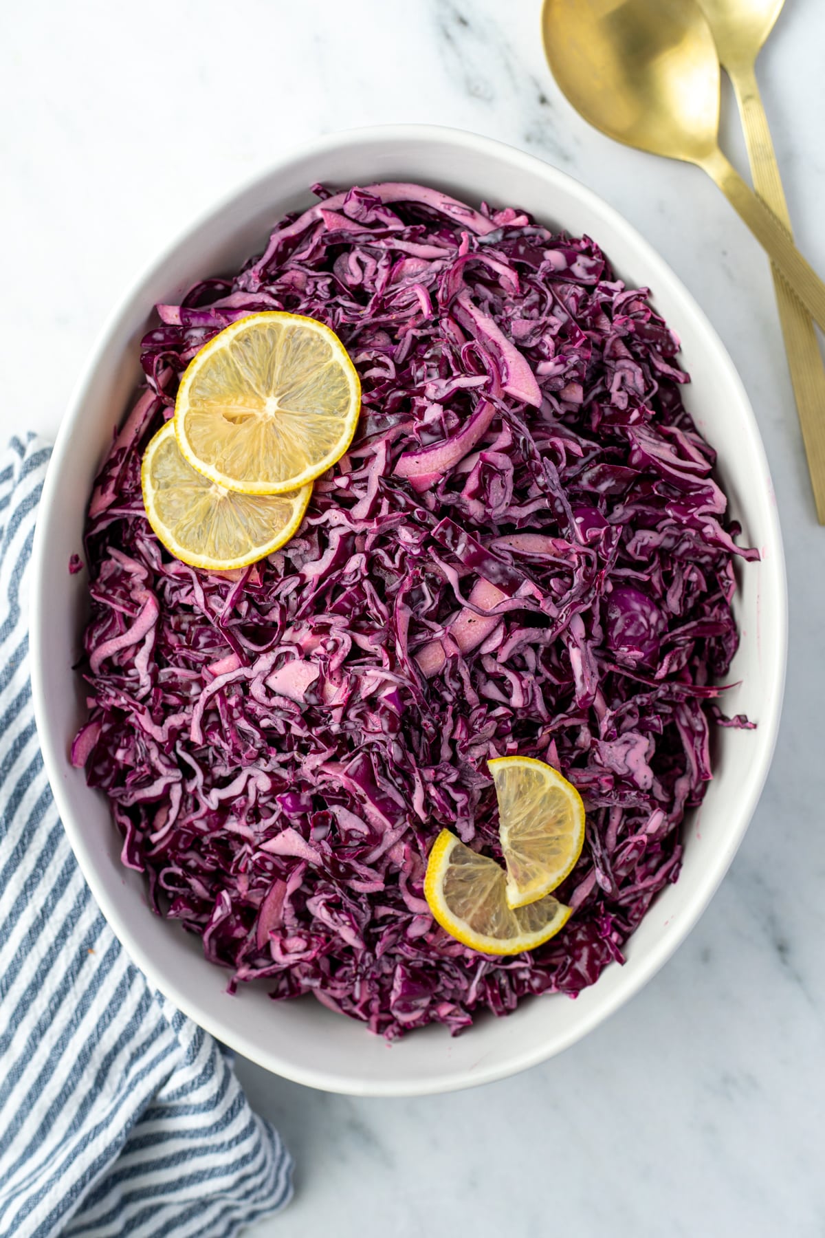 An oval bowl containing red cabbage salad and topped with fresh lemon slices.