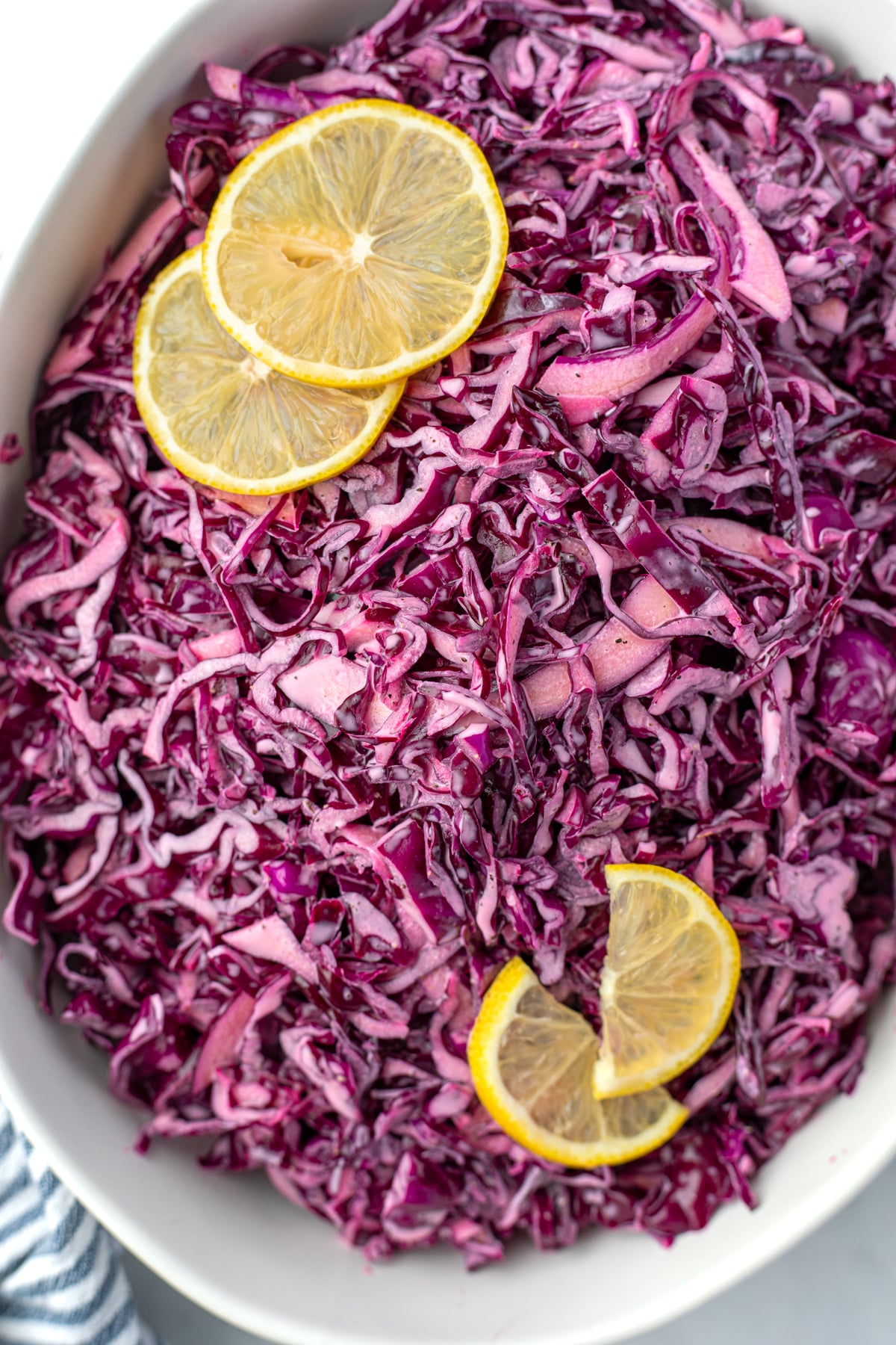 A bowl filled with red cabbage salad and garnished with lemon slices.