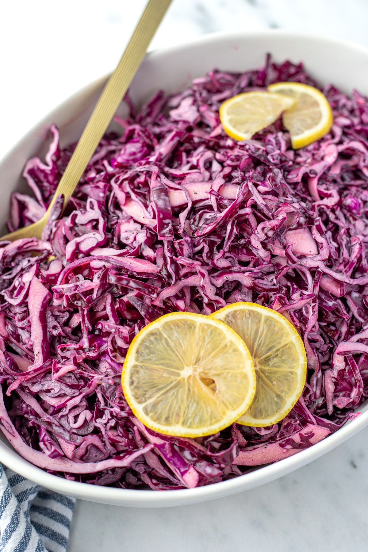 A spoon resting along the side of a oval bowl of red cabbage salad.