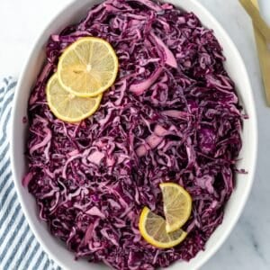 An oval bowl filled with red cabbage salad and garnished with lemon slices.
