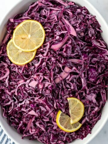 An oval bowl filled with red cabbage salad and garnished with lemon slices.
