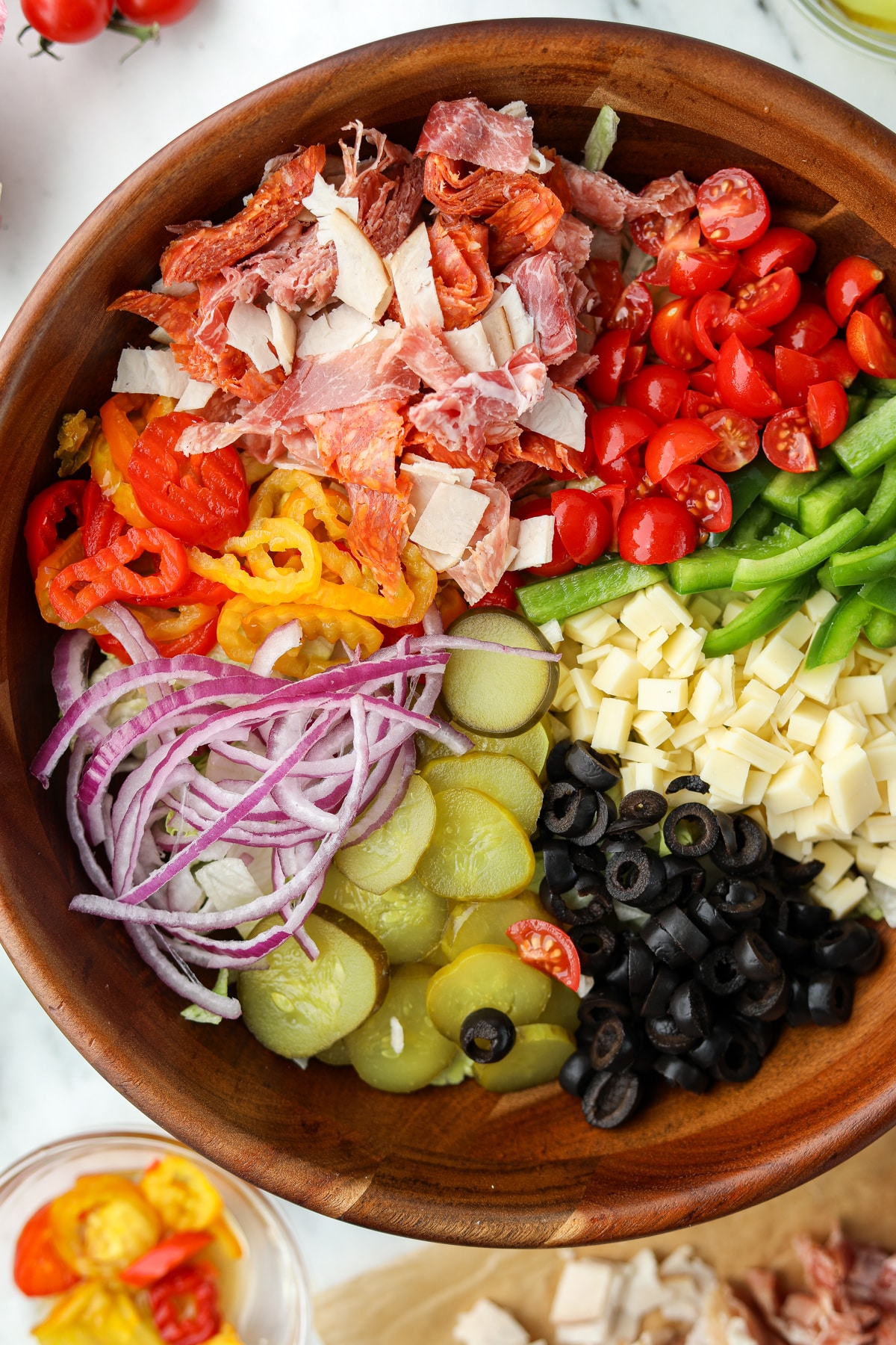 An overhead image of a large salad bowl filled with sections of toppings, including meat, cheese, pickles, etc.