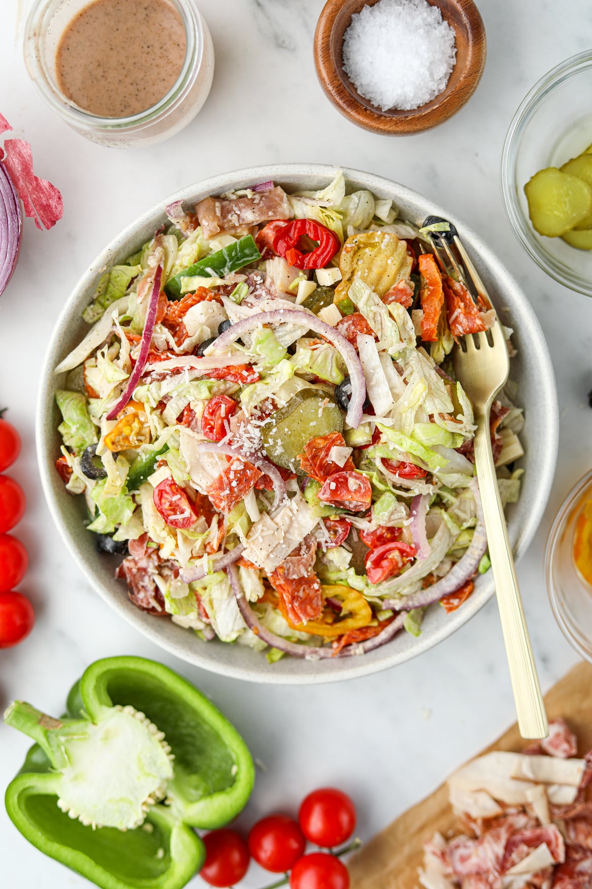 An bowl of salad topped with pickles, red onion, and parmesan cheese.