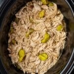 A slow cooker filled with shredded chicken and topped with pepperoncini peppers.